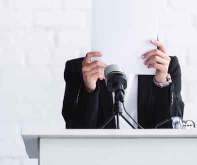 young lecturer, suffering from fear of public speaking, standing on podium tribune and hiding face