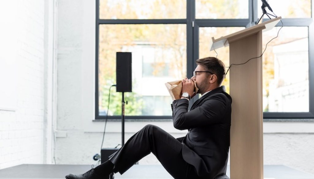 side view of scared businessman in suit breathing in paper bag during conference