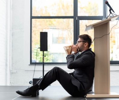 side view of scared businessman in suit breathing in paper bag during conference